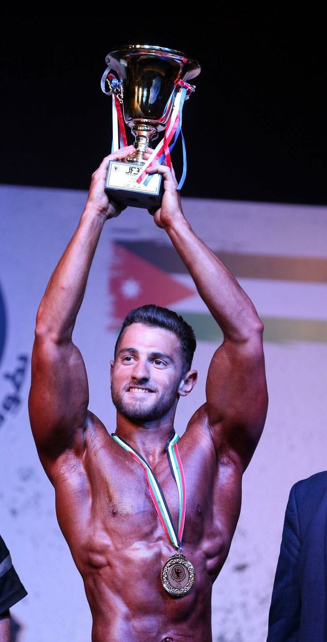 Basel Tayyan holding a championship trophy on stage in Jordan